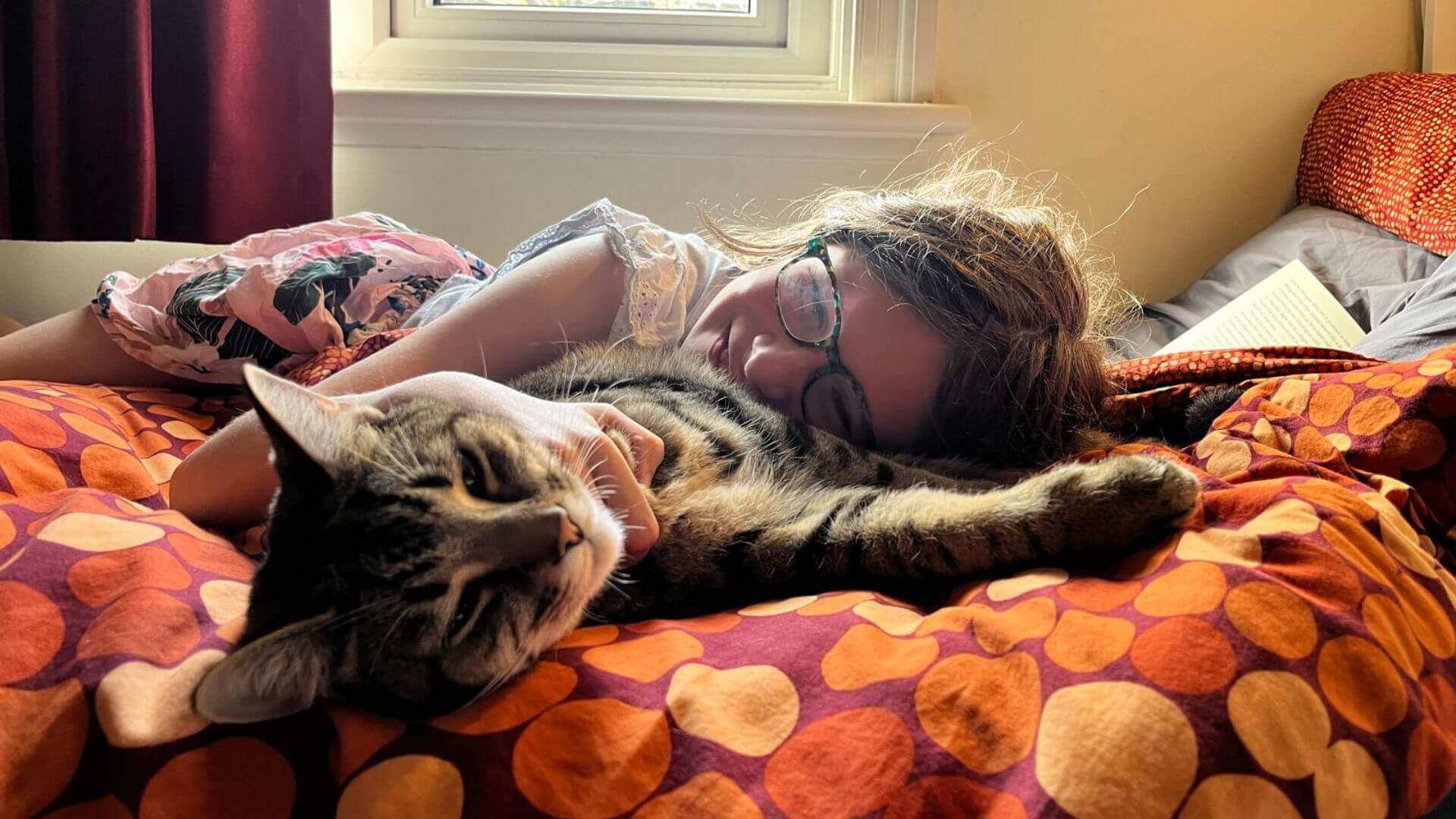 girl and cat laying on bright blanket